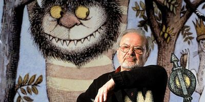 Maurice Sendak sitting in front of a large Wild Things picture