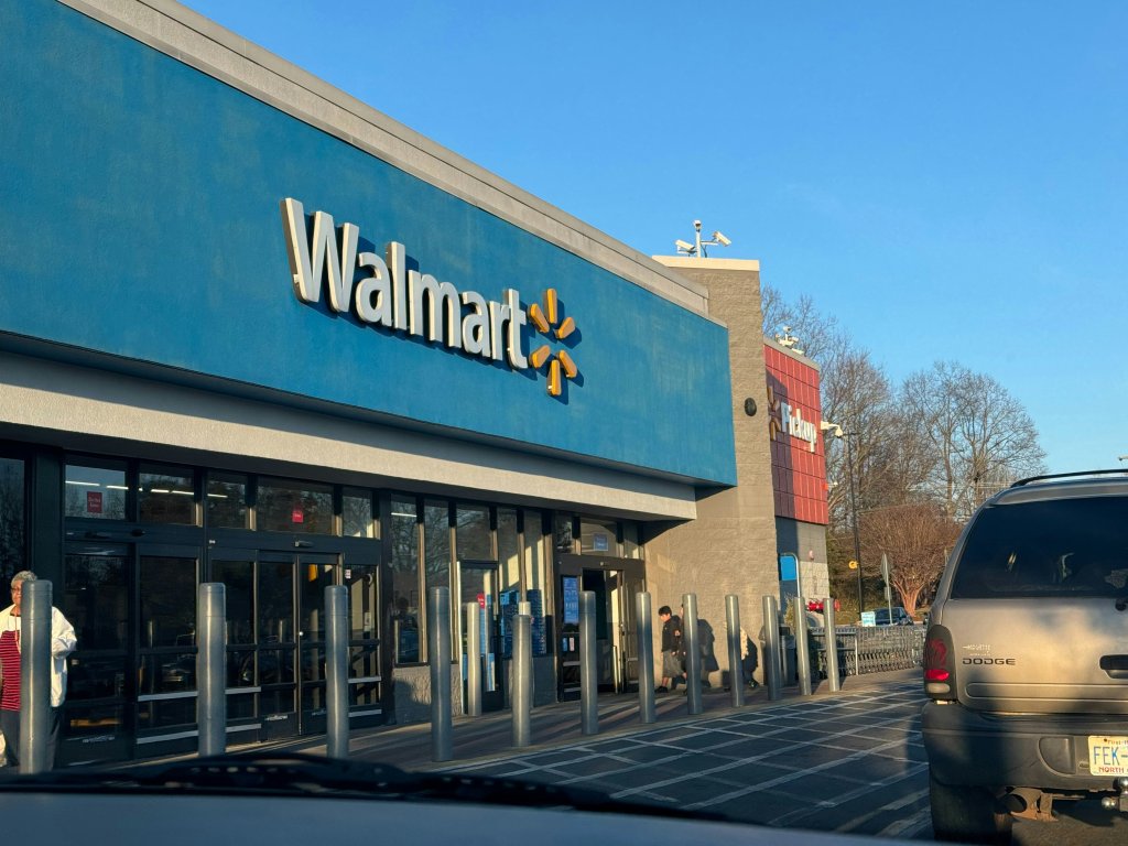 Walmart store entrance with a blue sign and parked cars in daylight.