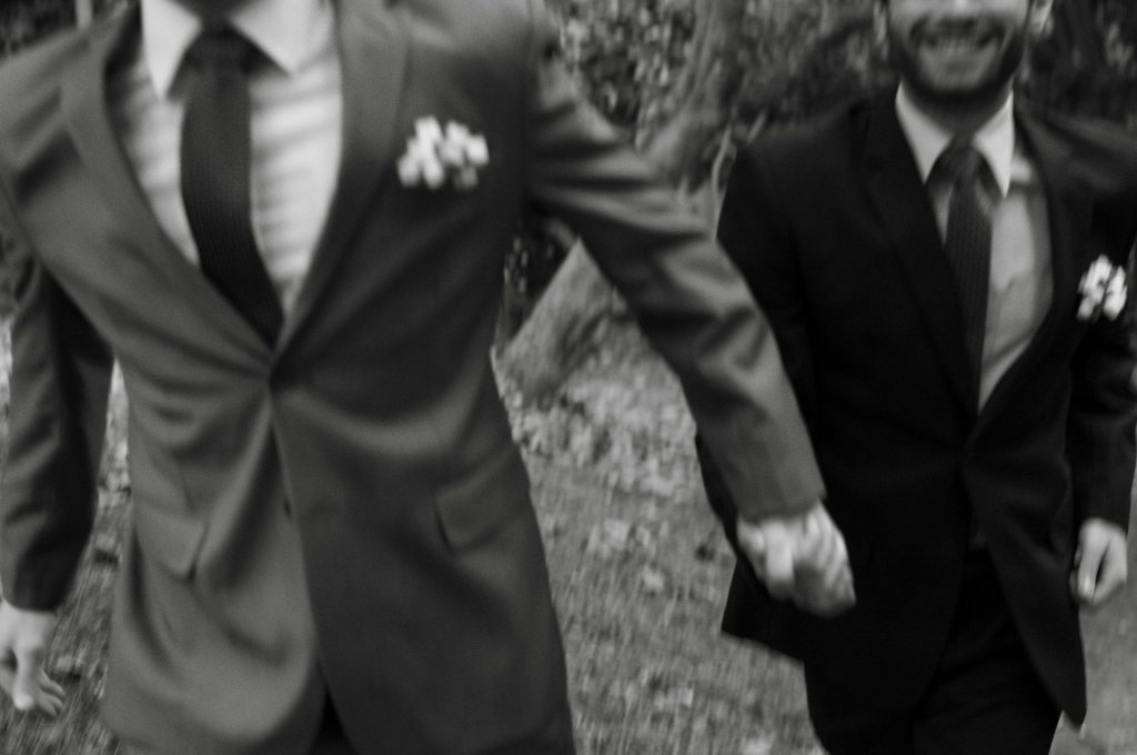 Two people in suits holding hands while walking, captured in motion blur, black and white image.