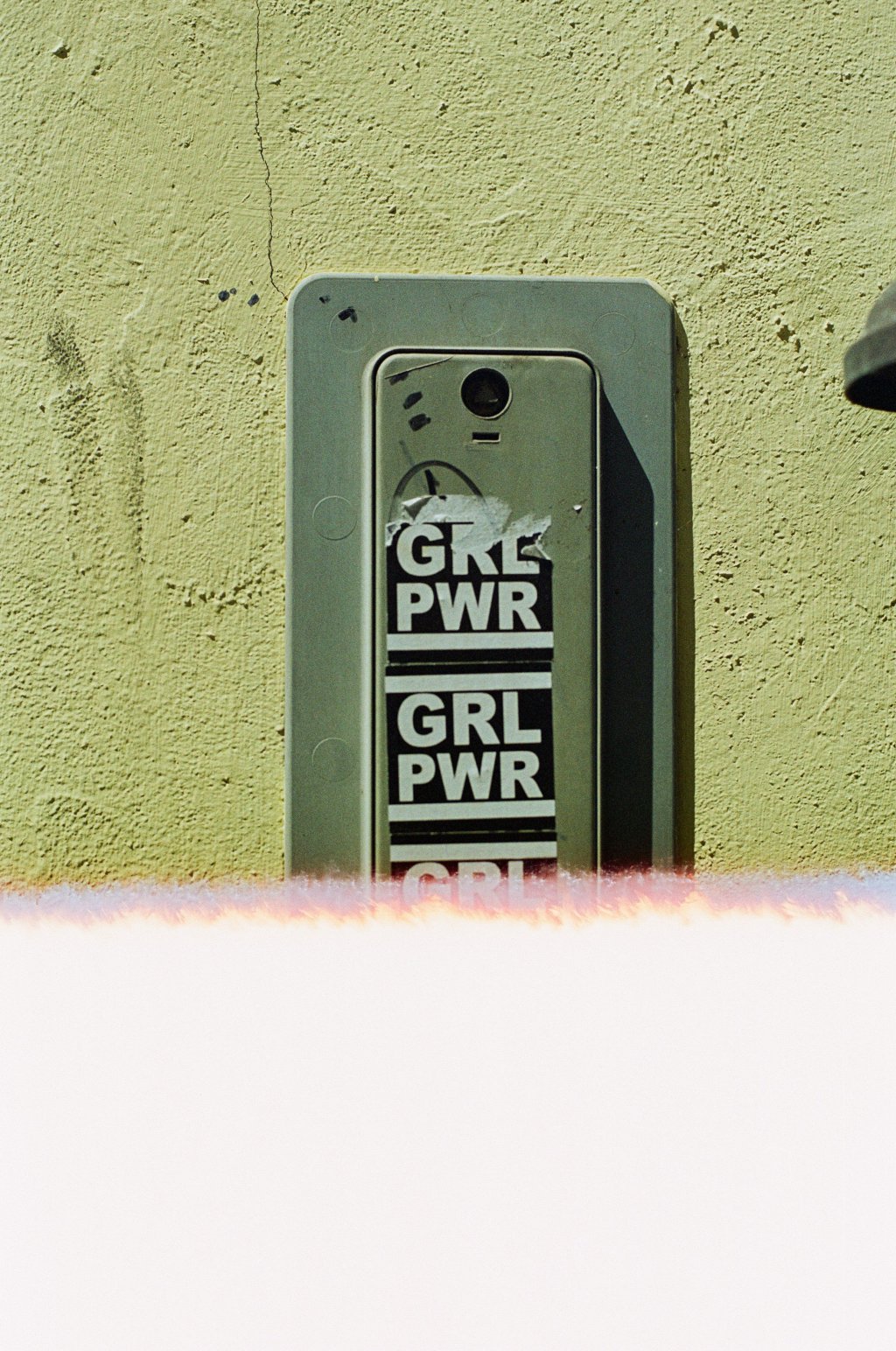 Intercom on wall with "GRL PWR" stickers and a light leak at the bottom.