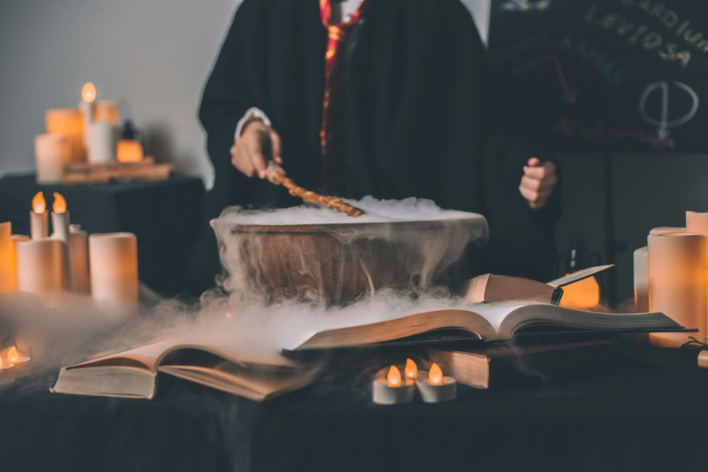 Person in robe stirring smoky cauldron, surrounded by candles and open books.