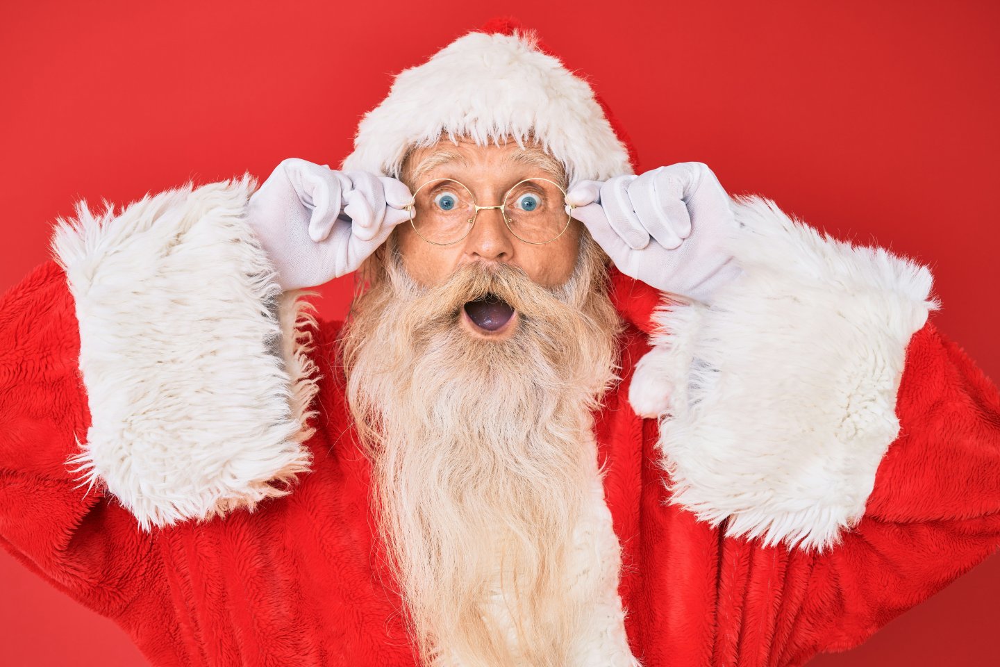 Surprised Santa with glasses, holding his frames, on a red background.