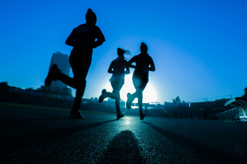 Silhouettes of three people jogging at sunrise on a track.