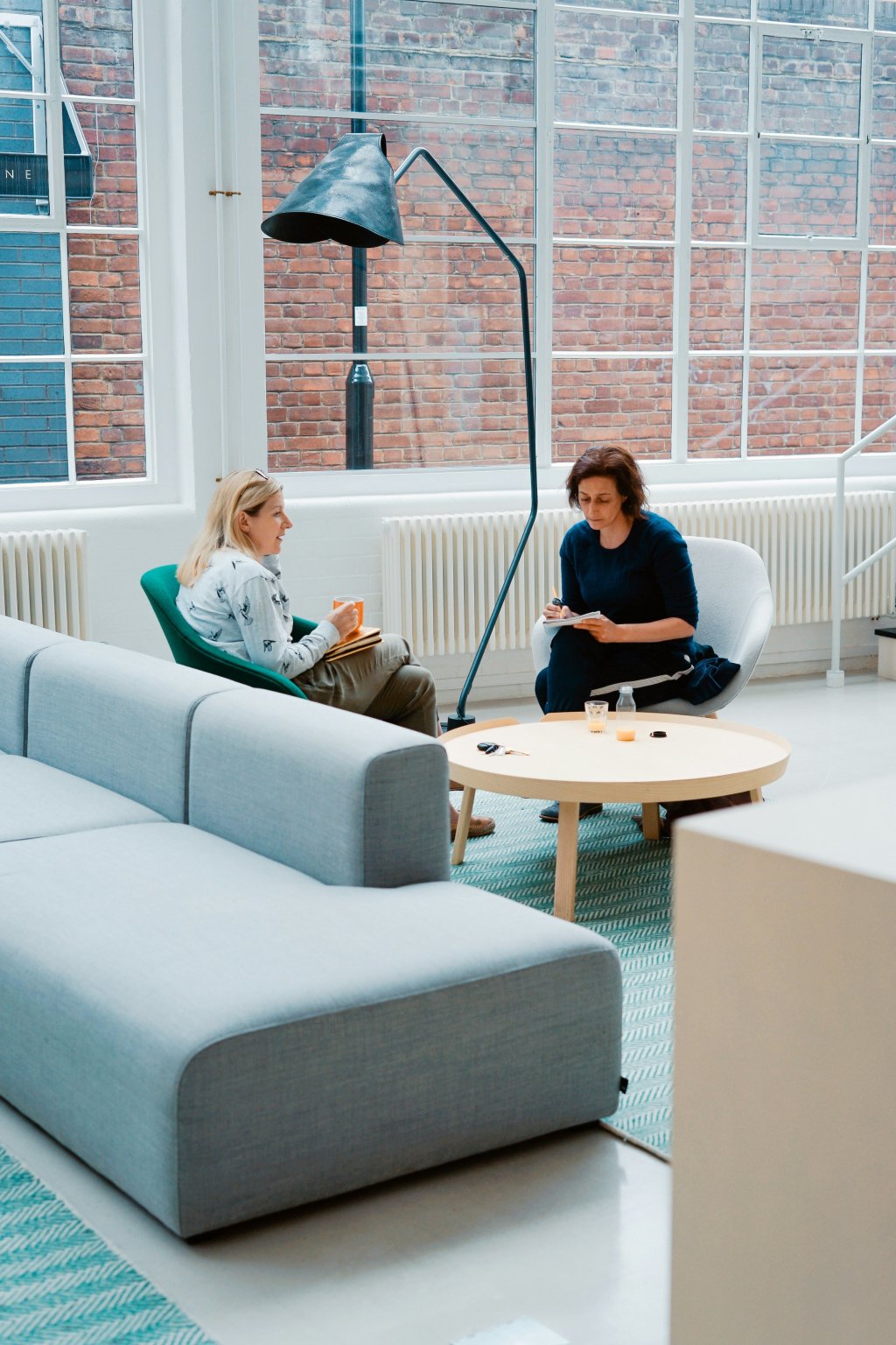 Two people sit and chat in a modern, light-filled office lounge.