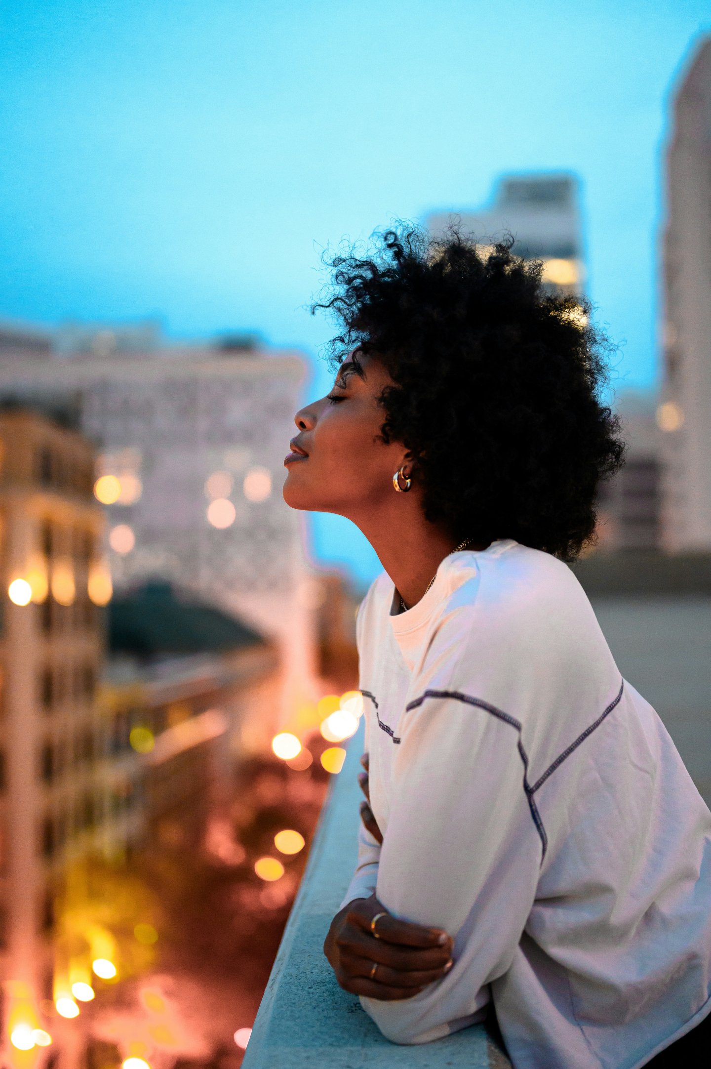 A black woman gazing over a cityscape from a rooftop at dusk.