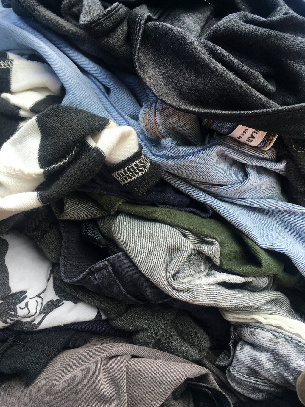 Pile of assorted clothes including denim, black, and striped fabrics.