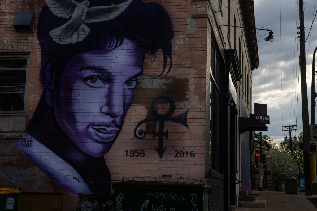 Purple mural of a prominent musician with a dove above, dates 1958-2016, on a brick wall.