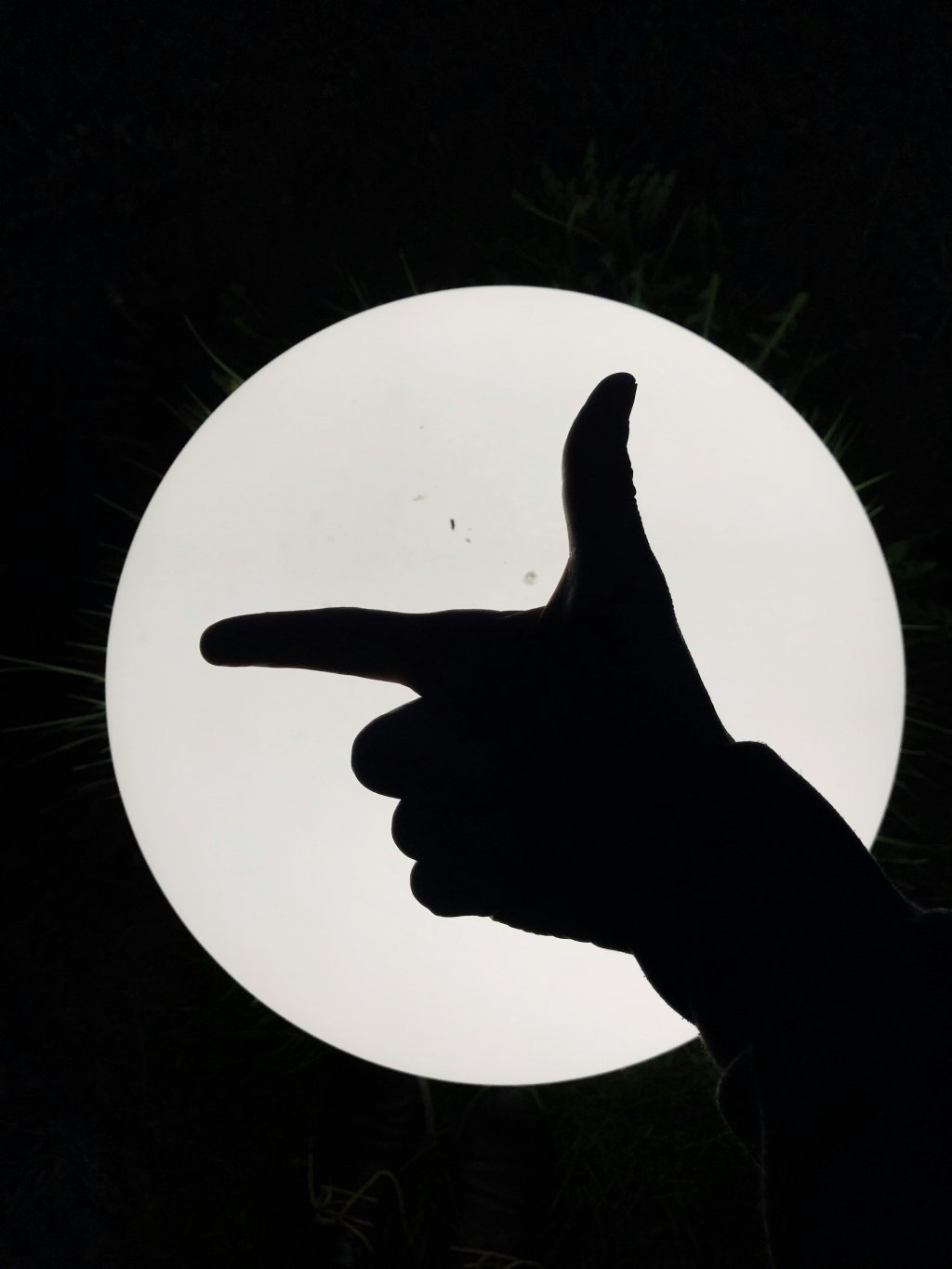 Silhouette of hand pointing like a gun against a bright, circular light source at night.