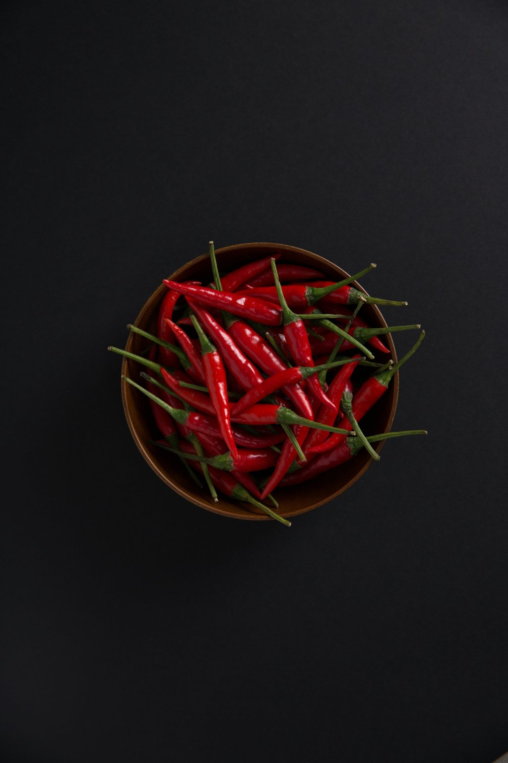 A bowl of fresh red chili peppers on a black background.