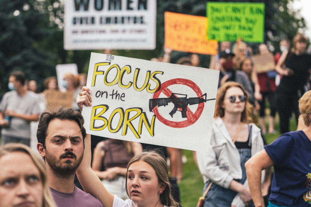 Protesters holding signs, including "Focus on the Born" with a crossed-out rifle image.