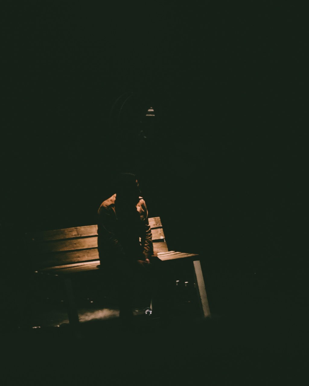 Person sitting alone on a dimly lit bench in the dark.