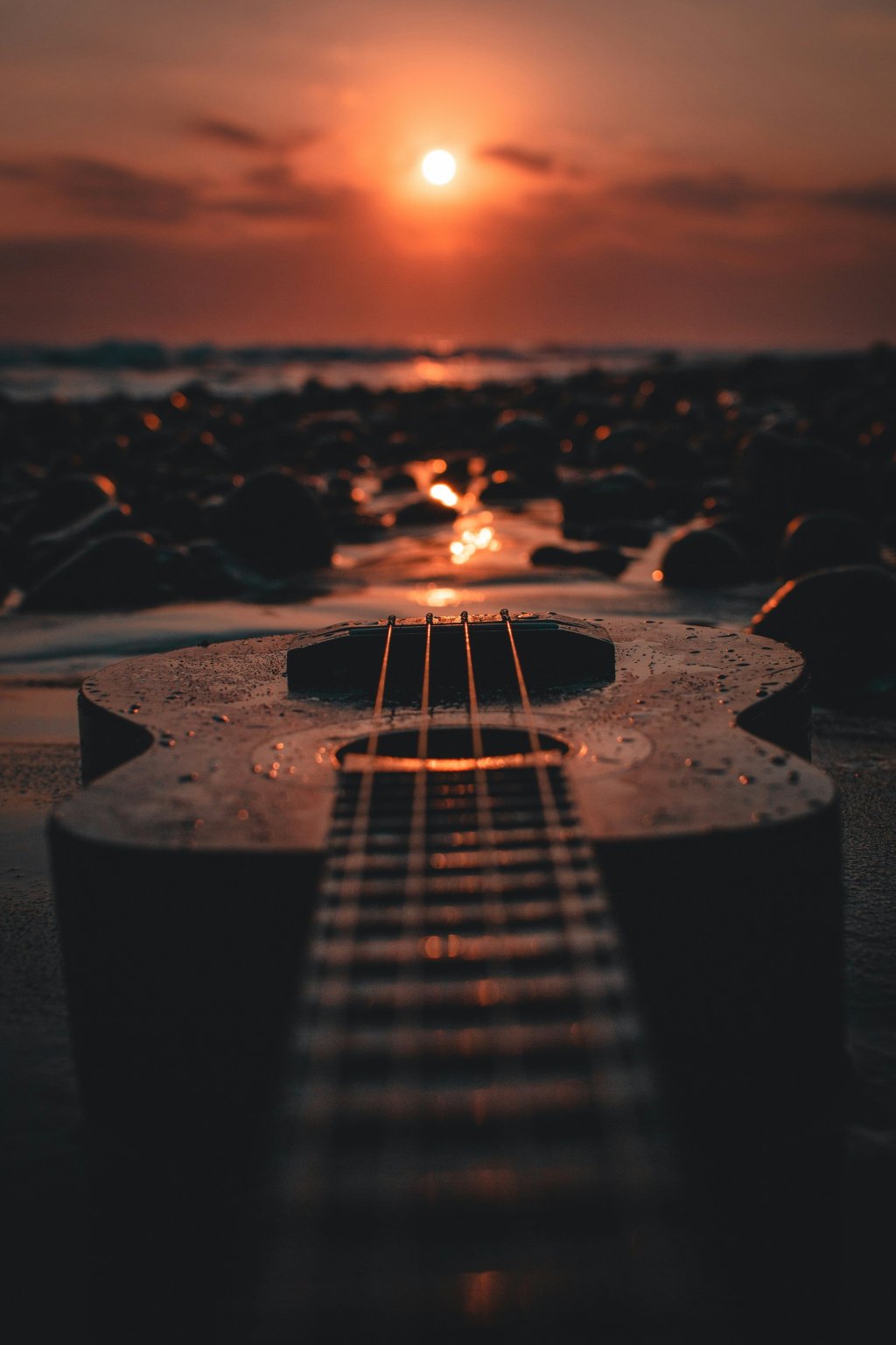 Guitar on a pebble beach at sunset, reflecting the warm glow of the sun.