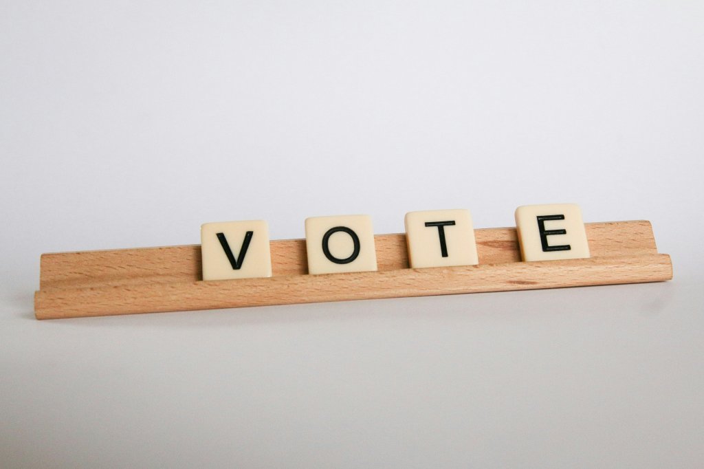 Tiles spelling "VOTE" on a wooden rack against a plain background.