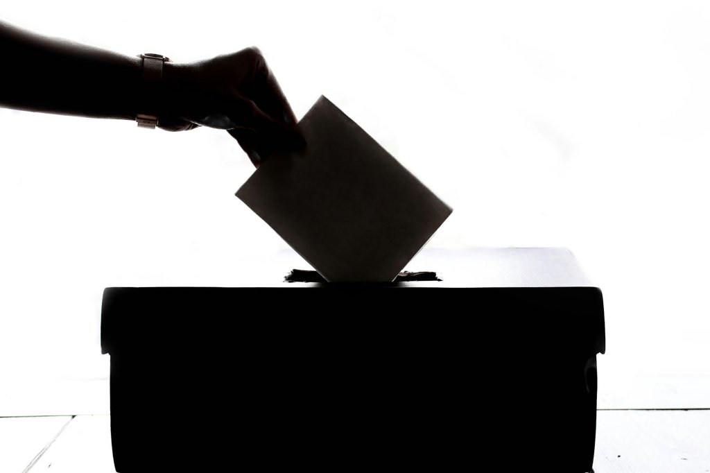 Silhouette of hand placing a ballot into a box.