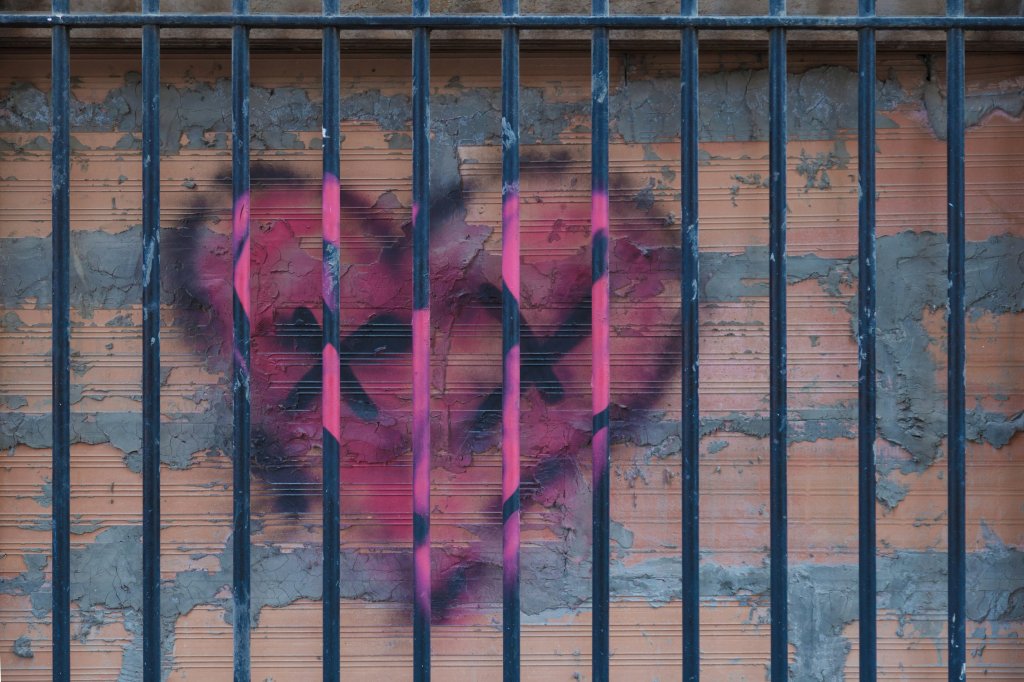 Pink heart graffiti behind metal bars on a weathered brick wall.