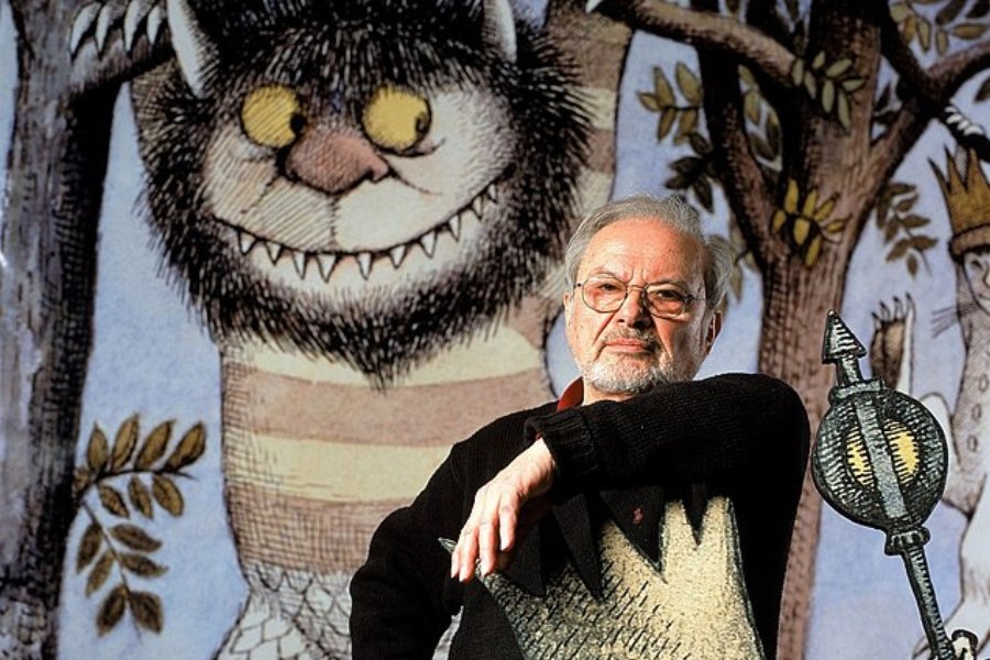 Maurice Sendak sitting in front of a large Wild Things picture