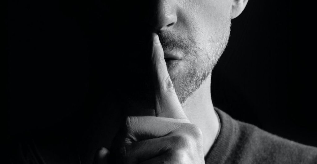 man holding finger to his mouth as a signal to be quiet