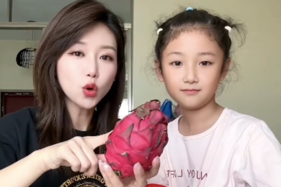a girl standing next to her mom who is holding a dragon fruit