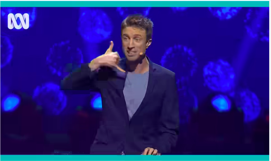 man on stage at the piano making a phone gesture with his hand