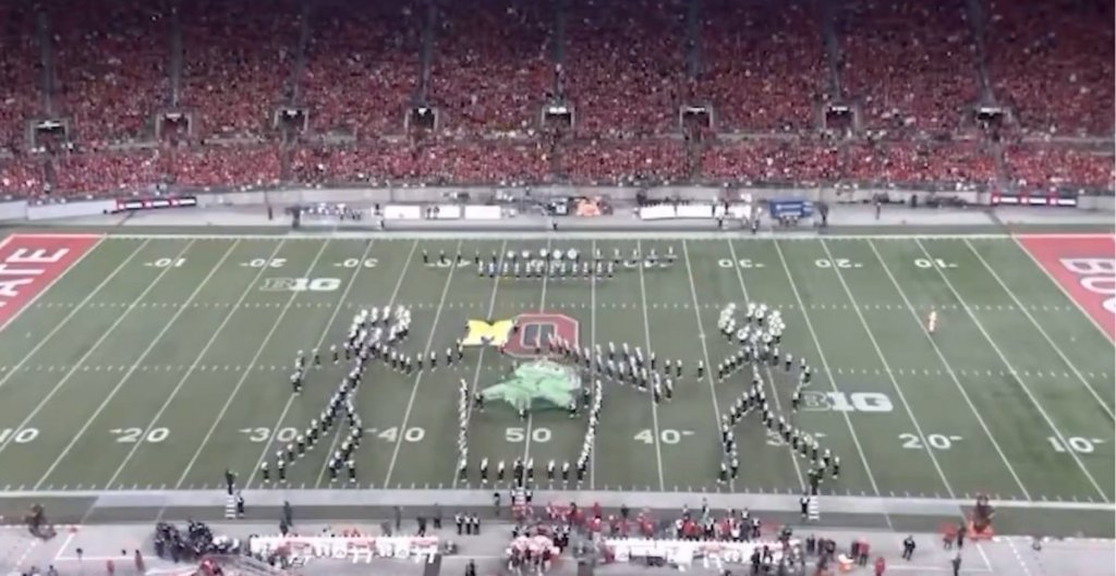 marching band members arranged to look like a person taking the lid off at trash can and another person throwing the Michigan flag into it