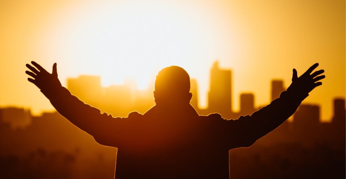 man standing with his arms raised, facing the rising sun