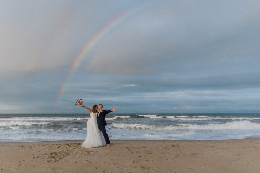 bride and groom on beach in front of rainbow