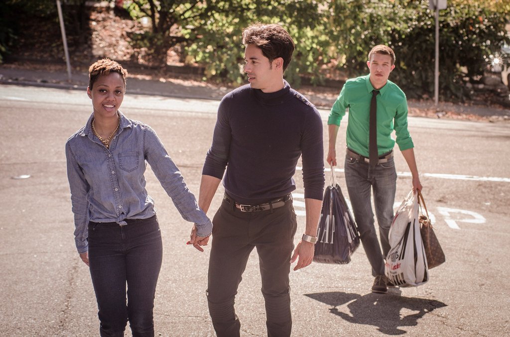 Couple holding hands, while a man behind them carries shopping bags.