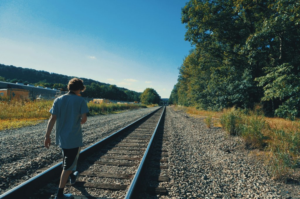 a boy standing on a train track next to a forest