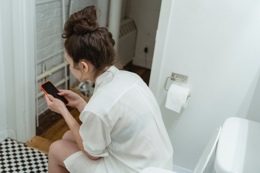 woman using phone on the toilet