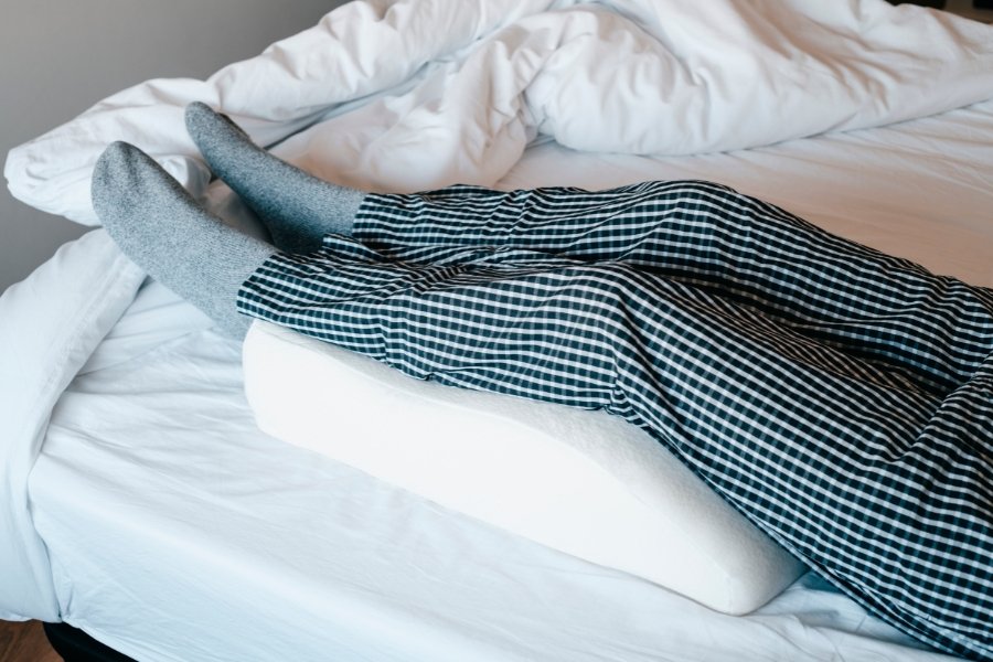 person in bed with legs up on a pillow