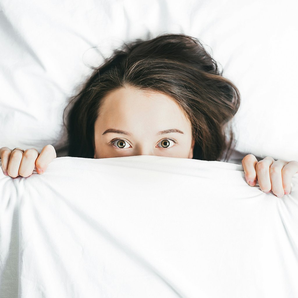 a woman holds a bedsheet up to her eyes