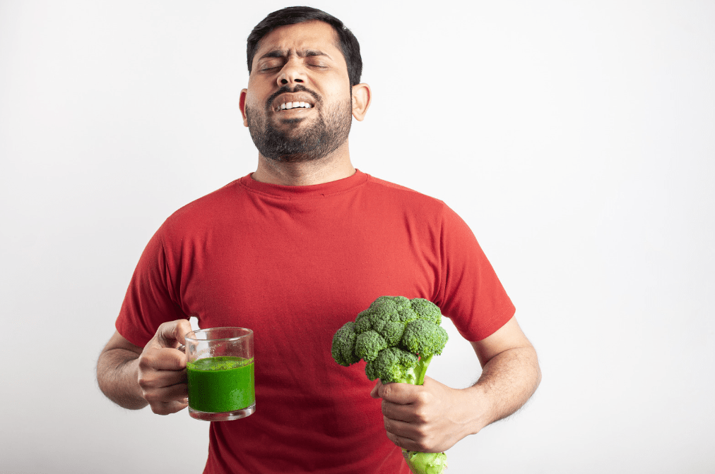 Man with broccoli and green smoothie and he's not happy about it.