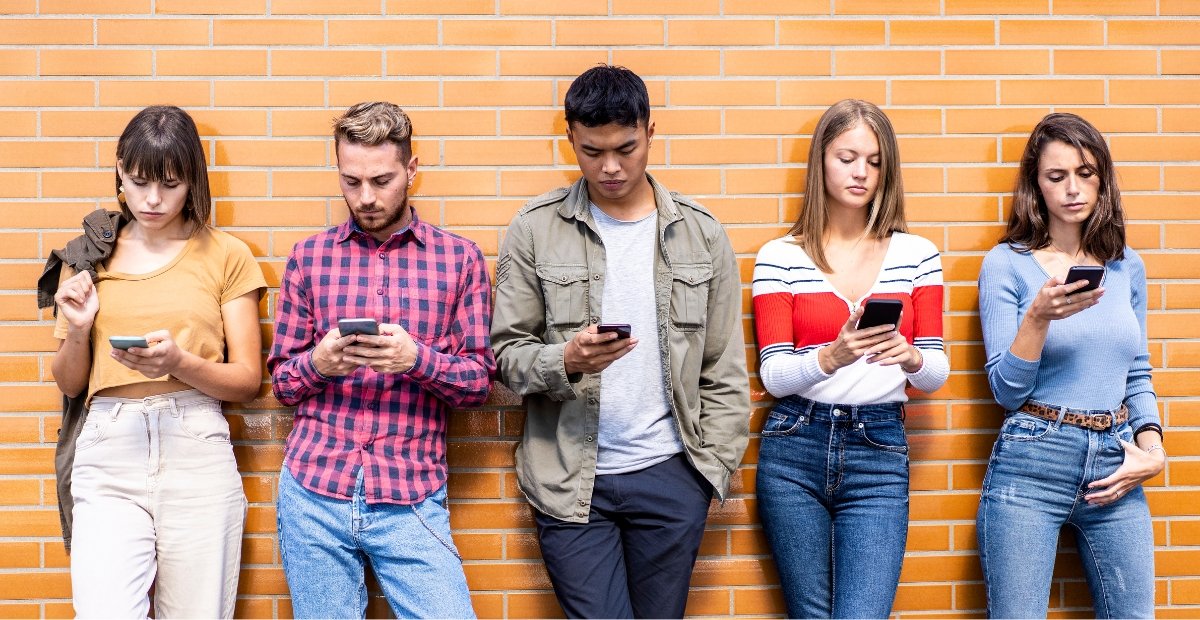 five young adults standing looking at their phones