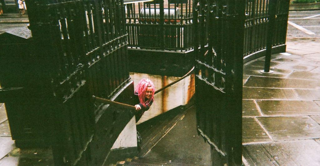 woman with bright pink hair peeks around a stairwell
