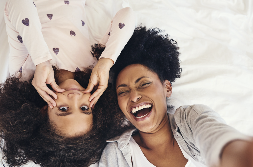 A woman laughs at her daughter making a goofy face for a selfie