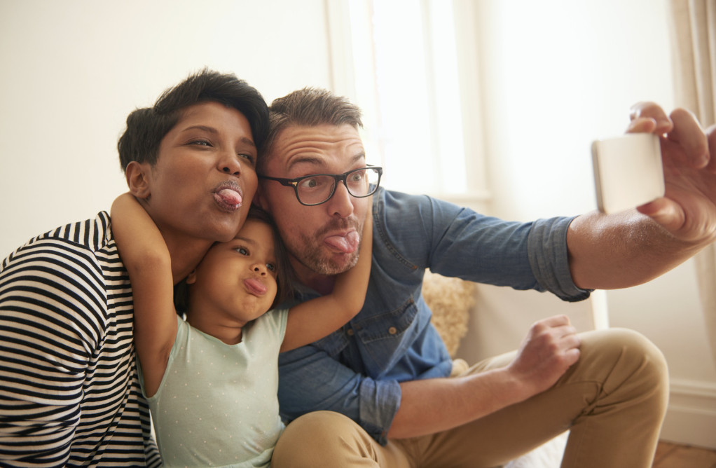 A family of two parents and one child stick their tongues out while taking a selfie.