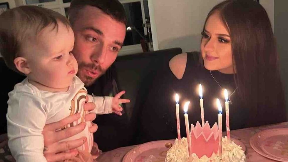 mom and dad holding baby in front of a birthday cake