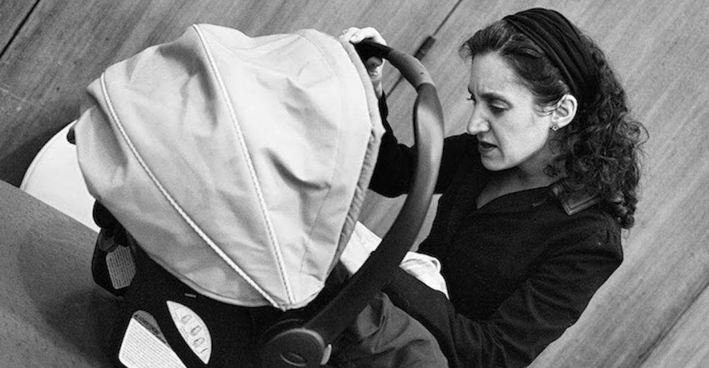 Black and white photo of woman looking into a baby carrier