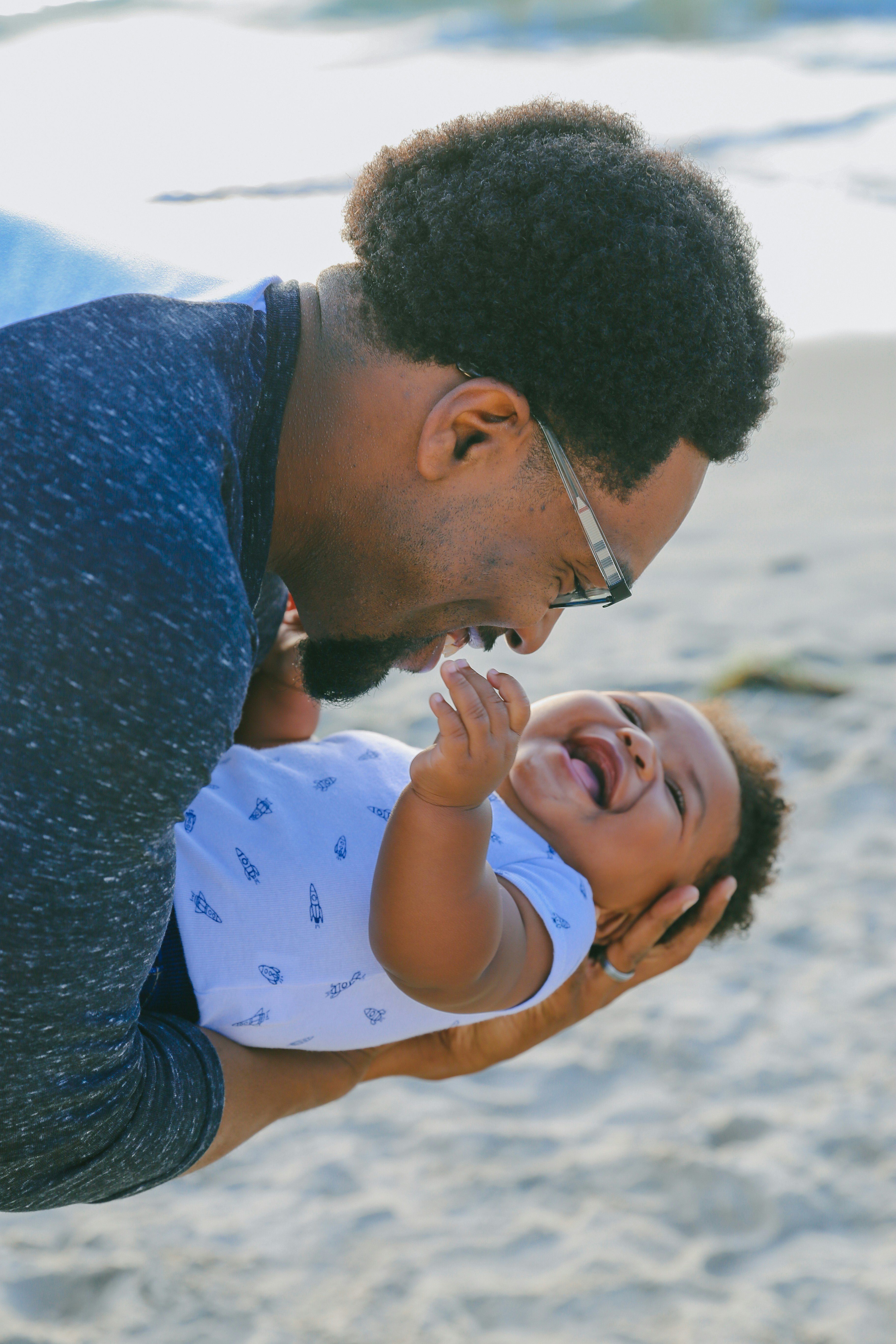 man in blue sweater kissing baby in white and blue polka dot shirt on beach during