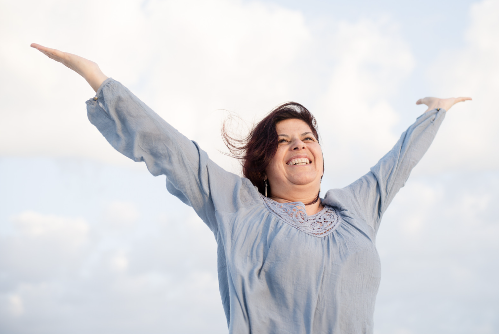 A larger woman with her arms out and smiling outside