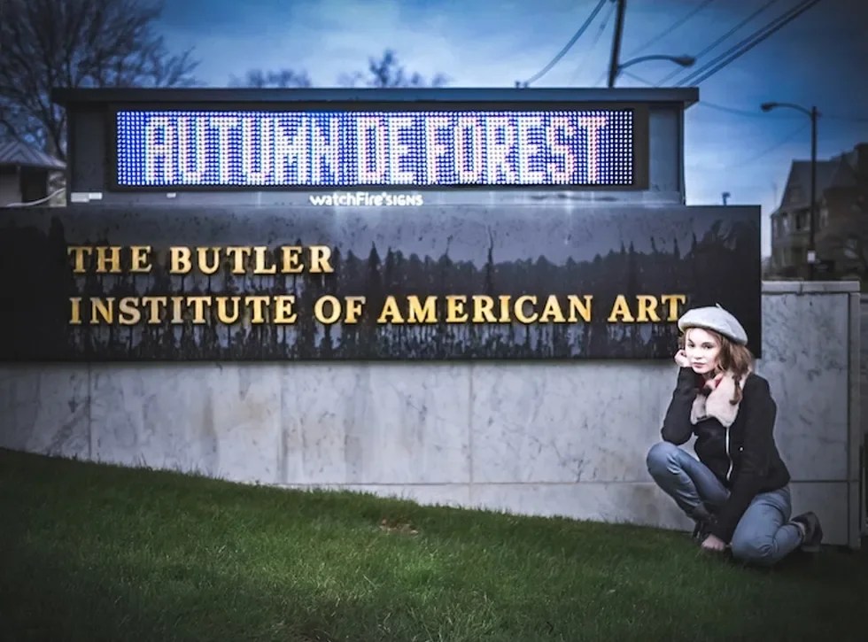 Woman kneeling beside Butler Institute sign with 