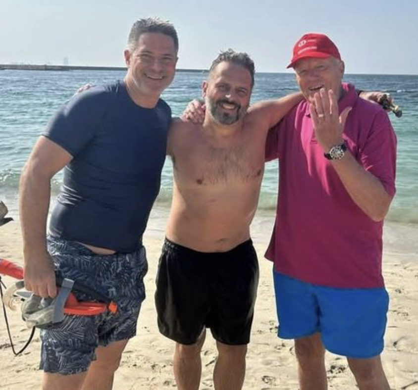 Three men posing with one man holding up his hand to show off his wedding ring.