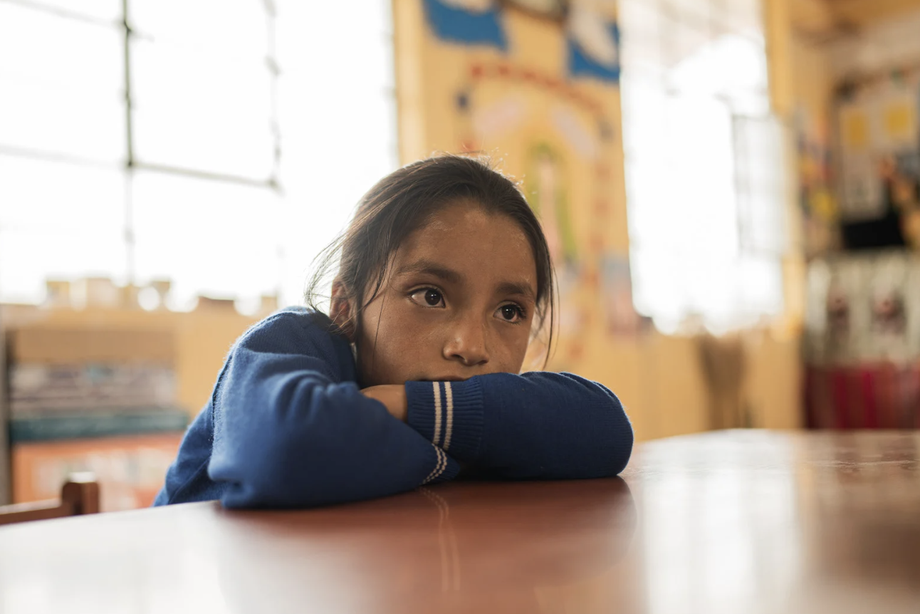 a little girl leans on her arms on her desk 
