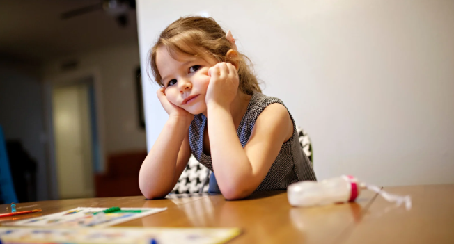 a young girl sitting at a table looking sad