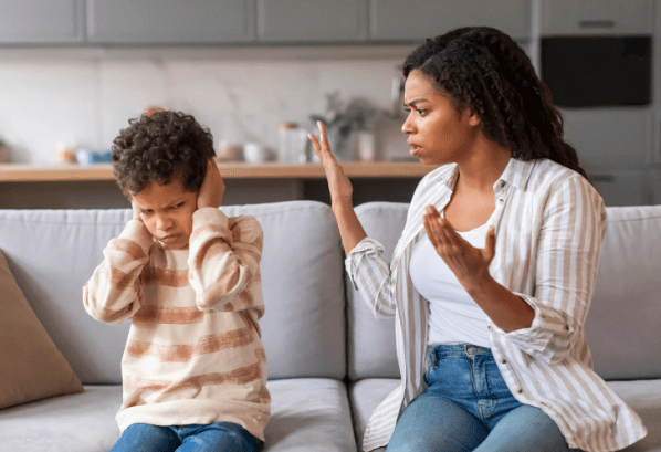 A child covers his ears while his mother looks at him in frustration