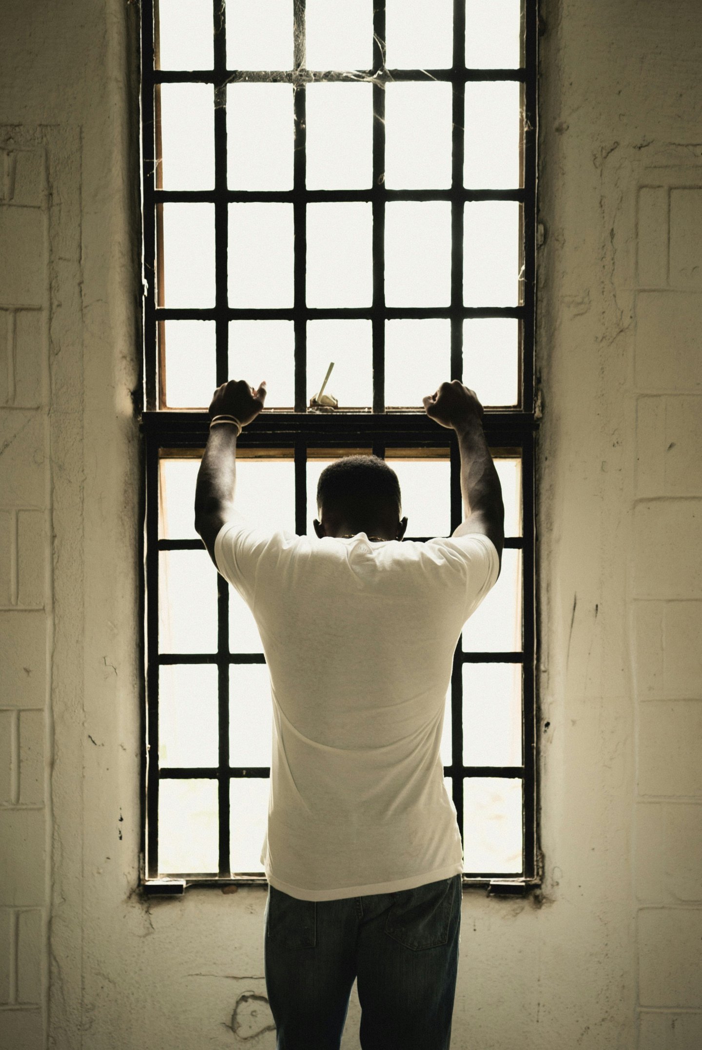 man with his back to camera places arms on barred jail window