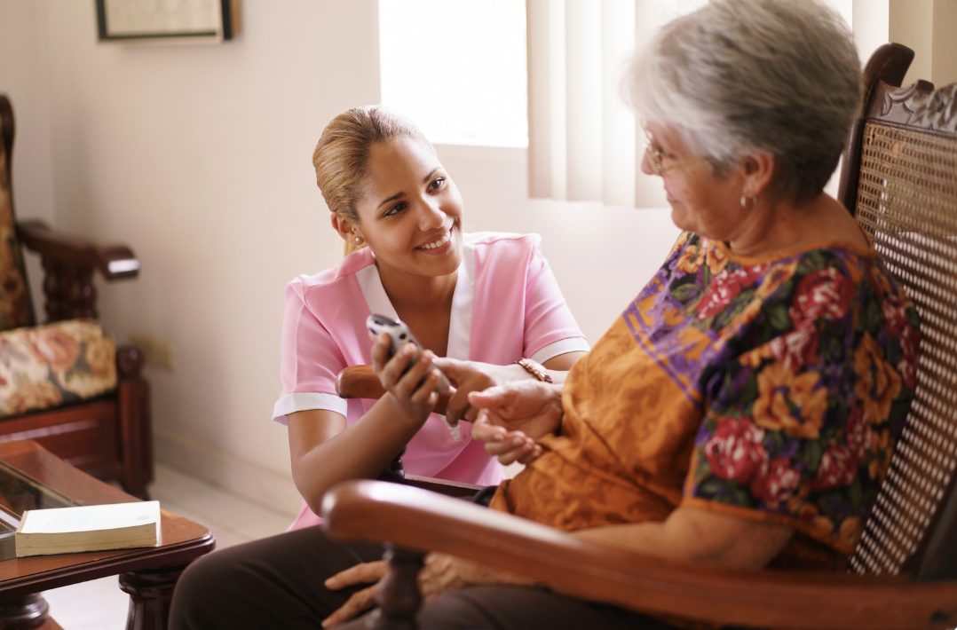 hospice nurse shows elderly woman in chair something on her phone