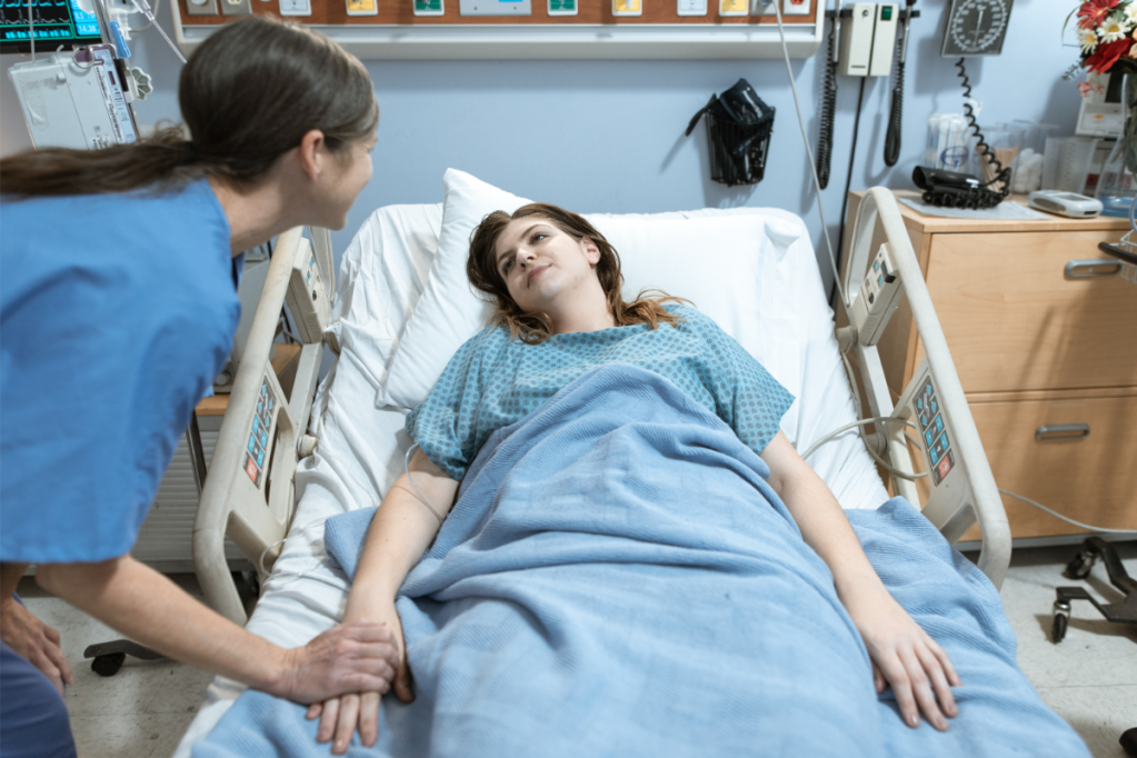 nurse leans over patient in a hospital bed and holds her hand