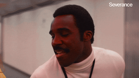 Man in a white turtleneck smiling and laughing in an office hallway.