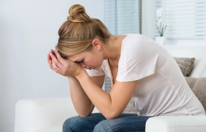 stressed mom, young mom, stressed millennial, woman hands on her head, woman on couch
